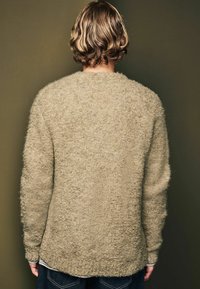 Tekstureret, olivengrøn oversized sweater med en fluffy overflade, sænkede skuldre og en rund bund, båret over en hvid langærmet skjorte.