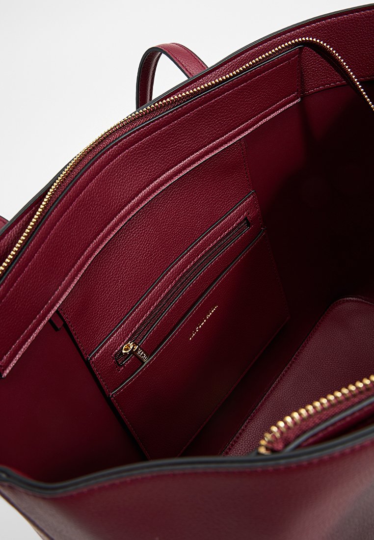 Interior de un bolso de piel burdeos con compartimento con cremallera, bolsillo tipo deslizante y acentos de hardware dorado, que presenta una textura lisa y un diseño estructurado.