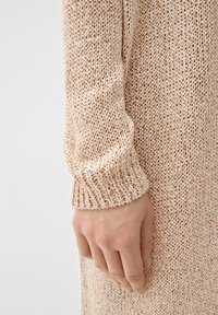 Manica di un maglione lavorato a maglia beige con polsino a costine, che mette in evidenza un motivo testurizzato e una vestibilità morbida, evidenziando l'aspetto leggero del tessuto.