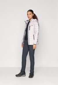 Világosszürke puffdzseki kapucnival, cipzárral és oldalsó zsebekkel. Fekete toppal és sötétszürke nadrággal párosítva. Fekete túracipők.