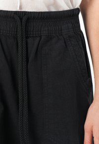 Zwarte katoenen shorts met een elastische tailleband, gevlochten koord en zijzakken. De stof ziet er zacht uit met een matte afwerking.
