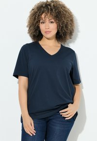 T-shirt bleu marine en V en tissu doux avec des manches courtes, associé à un jean bleu foncé pour un look décontracté. Design simple, sans motifs supplémentaires.