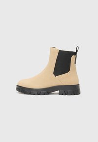 Botines de ante beige con un panel lateral elástico negro, suela texturizada y una lengüeta trasera para ponerlos fácilmente. Diseño grueso y robusto.