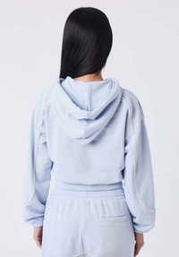 Lichtblauwe cropped hoodie met een capuchon, accentstiksels, lange mouwen, en bijpassende broek, met een elastische tailleband en achterzak.