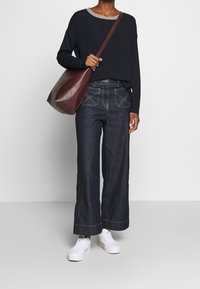 Svart långärmad topp med randig halsringning, kombinerad med vida mörka denimjeans. En brun läderhandväska och vita sneakers fulländar looken.