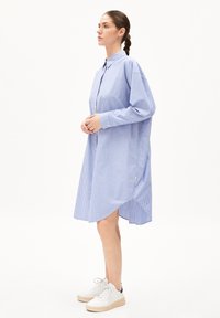 Robe chemise à rayures bleues et blanches, dotée d'un col, d'une fermeture à boutons, de manches longues et d'un ourlet arrondi. Portée avec des baskets blanches.