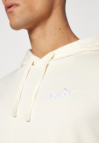 Felpa crema con cappuccio e coulisse, caratterizzata da un logo Puma ricamato in azzurro chiaro sul petto. Tessuto morbido e design dal taglio relax.