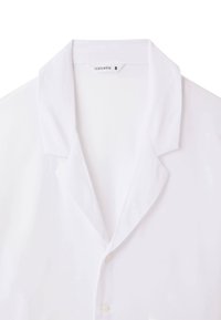 Camicia bianca con colletto, realizzata in tessuto morbido. Presenta una vestibilità standard e una leggera lucentezza, senza motivi o accenti visibili.