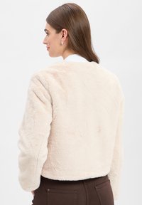 Licht beige nepleren jasje met een cropped ontwerp, een relaxte pasvorm en lange mouwen. Zachte textuur zonder zichtbare sluitingen.