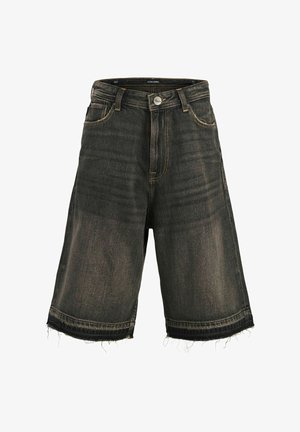 Garçon souriant debout portant une chemise à manches courtes à motifs, un t-shirt blanc, un short sombre au genou, des chaussettes blanches et des chaussures marron sur fond blanc.
