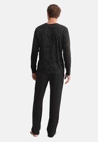 T-shirt à longues manches noir avec de grandes lettres graphiques dans une couleur contrastée, associé à un pantalon noir. Fabriqué en matériau doux et léger.