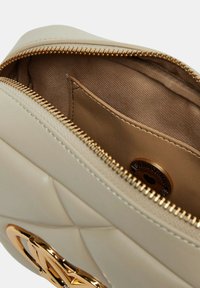 Borsa a mano in pelle beige con motivo trapuntato, chiusura con zip e un accento logo in tonalità oro. L'interno presenta un rivestimento in tessuto liscio.