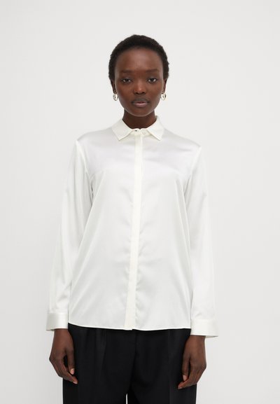Blouse en satin blanc avec un col pointu, des manches longues et une fermeture à boutons à l'avant, présentant une texture lisse et une coupe décontractée.