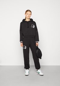 Black cropped hoodie with logo, matching joggers, and white sneakers. The outfit features striped accents and a textured fabric.