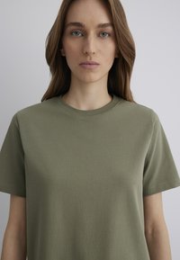Olive green cotton t-shirt with a rounded neckline and short sleeves, featuring a smooth texture and clean lines.