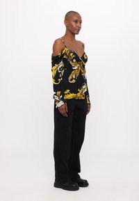 Juodas gėlių raštas, ilgomis rankovėmis, su off-shoulder dizainu. Juodos plačios kelnės ir masyvūs juodi batai. Sklandus audinys su ryškiais geltonais ir baltais akcentais.