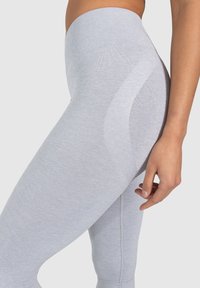 Leggings de color gris claro con una cinturilla acanalada y una textura suave, que presentan un sutil acento con patrón en el costado. Vista cercana del ajuste.