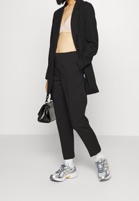 Svart kavaj över en nude-bra, kombinerat med skräddarsydda svarta byxor och silverfärgade löparskor. Håller en liten svart handväska.