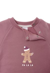 Light pink sweatshirt with a round neckline, featuring snap buttons. It has a gingerbread man graphic and the text "FA LA LA."