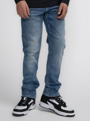 Jeans in denim azzurro chiaro con taglio dritto, abbinati a scarpe sportive nere e bianche con finitura testurizzata e accenti a contrasto.