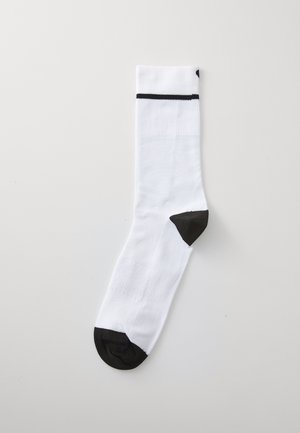 Chaussette blanche avec texture côtelée, accents noirs au talon et à la pointe, et une bande noire près du haut. Design athlétique standard, longueur moyenne.