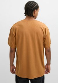 Camiseta de algodón marrón, diseño holgado con mangas cortas, cuello redondo, textura lisa y ajuste suelto. Sin patrones ni acentos.
