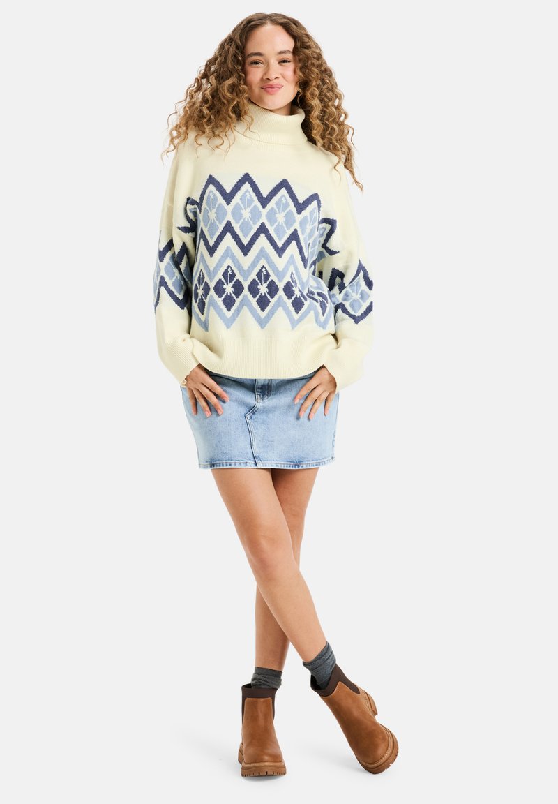 Knitted cream sweater with blue geometric patterns, mock neck design, paired with a light denim skirt and brown ankle boots.