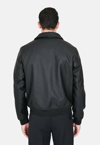 Giacca bomber in pelle nera con una texture liscia, colletto, polsini e vita a coste; presenta un design pulito e minimalista.
