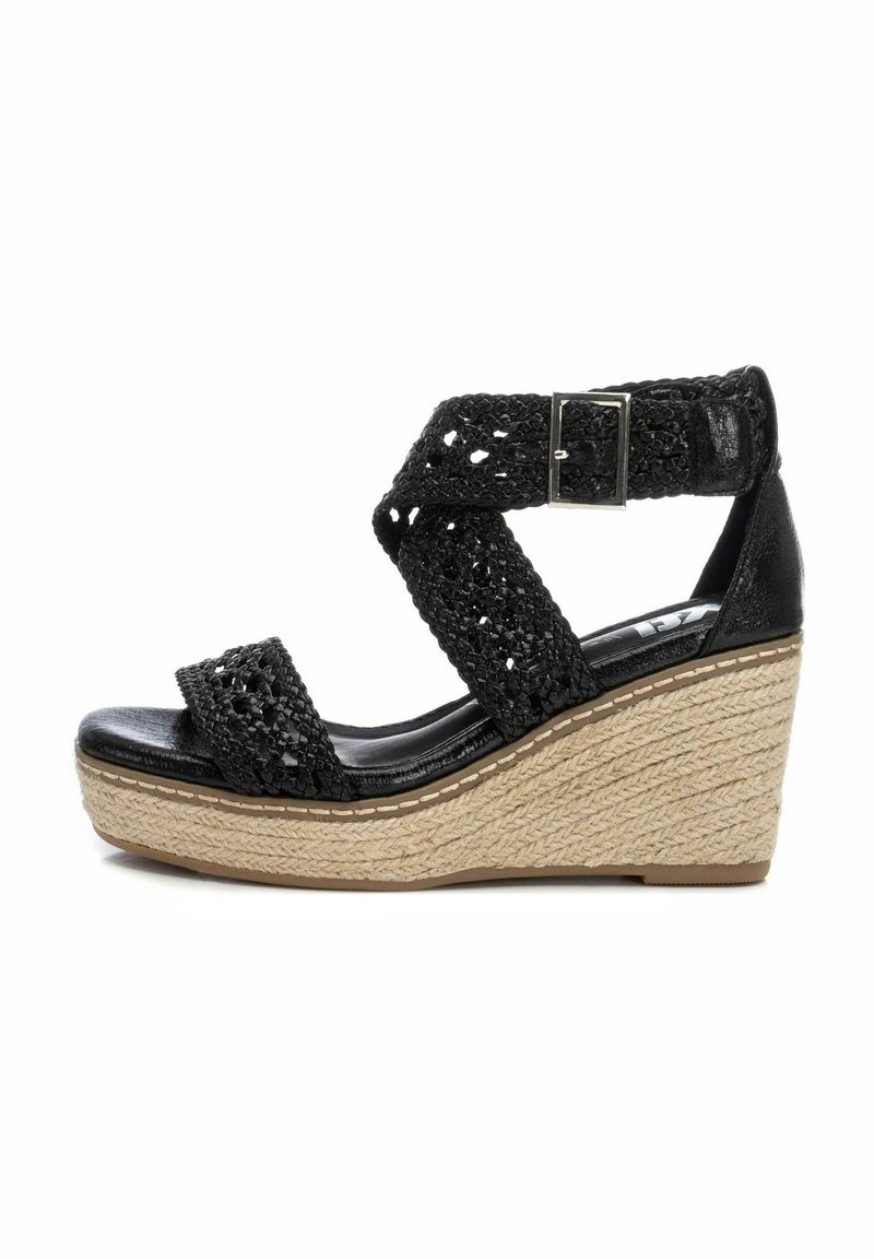 Sandalia de cuña negra con diseño de tira trenzada. Parte superior negra texturizada, hebilla ajustable al tobillo y plataforma envuelta en yute natural.