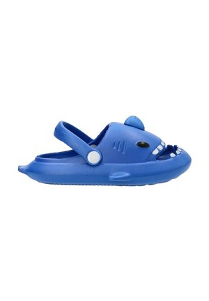Zuecos de plástico azules con forma de tiburón, boca sonriente, acentos blancos, correa lateral y forma redondeada. Suela texturizada para mayor agarre.