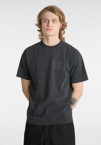 Svart bomulls-T-shirt med korta ärmar, rund halsringning och en liten, strukturerad Vans-logotyp på bröstet. Stylad med mörka byxor.