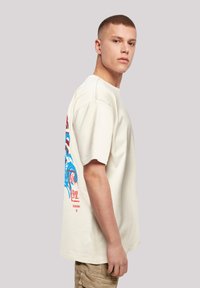 Korte mouwen crème katoenen t-shirt met een kleurrijke grafische print op de achterkant, voorzien van een relaxte pasvorm en geribbelde ronde hals.