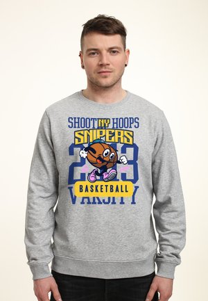 Man draagt een grijze trui met een cartoon basketbalfiguur en de tekst "Shoot NY Hoops Snipers 23 Basketball Varsity" op de voorkant.