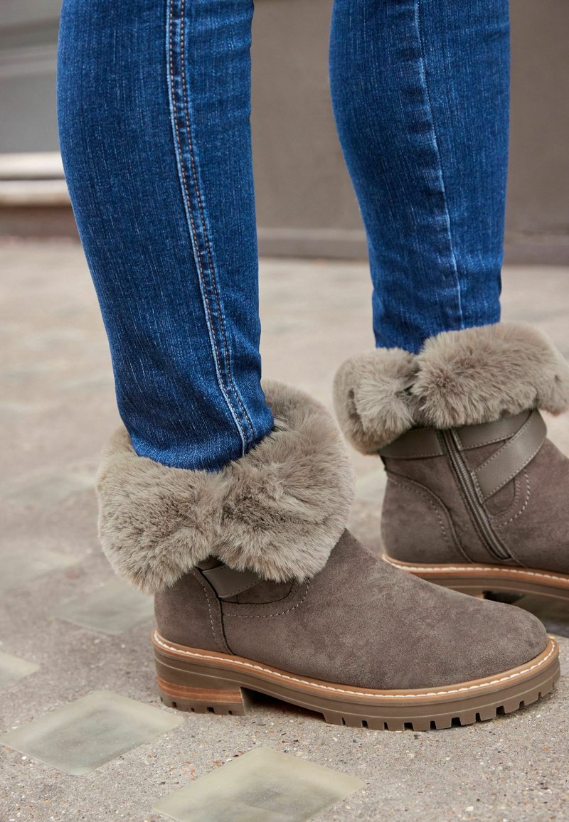 Graue Wildleder-Stiefeletten mit einem hellgrauen, plüschigen Kunstfellbund und einer braunen Gummisohle. Jeans mit einer blauen Denim-Textur und -Stichen.