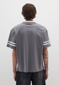 Camiseta de algodón gris con un corte relajado, que presenta acentos de rayas blancas en las mangas, el cuello y una textura suave.