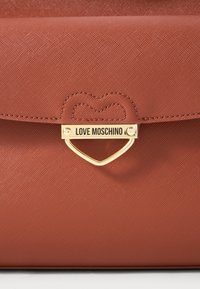 Smeđa teksturirana kožna torba s preklopom i zlatnim kopčanjem u obliku srca na kojem je ugravirano ime branda "LOVE MOSCHINO".