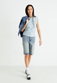 Un haut sans manches bleu clair associé à une veste en denim, un short en denim bleu clair, des chaussettes blanches et des chaussures noires avec des bandes blanches.