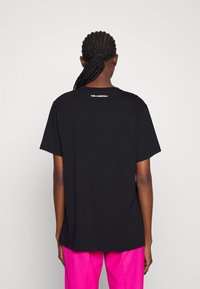 Camiseta de algodón negra con manga corta, presenta un cuello redondo y el logo en blanco "KARL LAGERFELD" impreso en la parte posterior del cuello. Diseño simple y clásico.