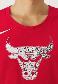 Camiseta deportiva roja con textura de malla, cuello redondo y un destacado gráfico de un toro en blanco y negro con un diseño pixelado. Incluye el logo de Nike.