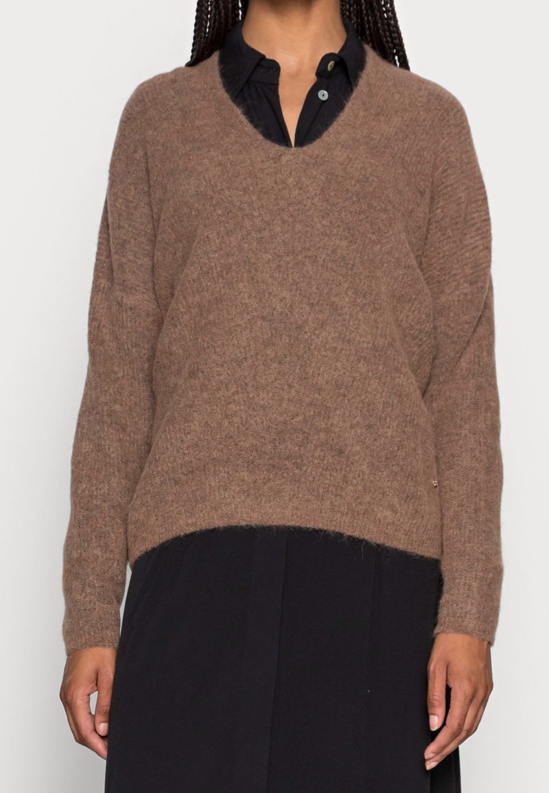 Maglione marrone a maglia con scollatura a V, maniche lunghe e vestibilità comoda. Texture morbida, abbinato a una camicia nera a bottoni sotto.