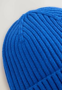 Berretto di maglia blu con una trama a costine, caratterizzato da strisce verticali e un risvolto. Il materiale sembra morbido e caldo.