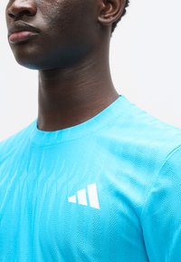 Μπλε αθλητική μπλούζα με υφασμάτινο σχέδιο, στρογγυλή λαιμόκοψη και λευκό λογότυπο της μάρκας στο αριστερό στήθος. Λείο ύφασμα, εφαρμοστή σχεδίαση.