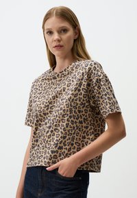 T-shirt à manches courtes en imprimé léopard beige et noir, avec une coupe décontractée et un col rond, associé à un jean en denim foncé.