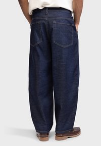 Jeans de denim largi, de culoare albastru închis, cu o textură netedă, cusături întărite și două buzunare aplicate pe spate. Asortați cu pantofi căprui.