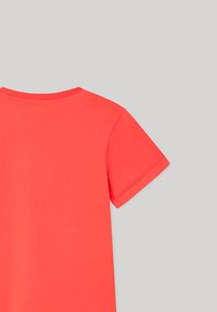 Camiseta de manga corta en color coral con cuello redondo, textura suave y diseño sencillo, que presenta dobladillos de mangas enrollados.