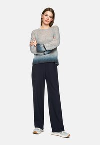 Leichtes Strickpullover in Grau-Blau-Gradient mit Glockenärmel; kombiniert mit schwarzen weiten Hosen und weißen Sneakers mit braunen Akzenten.