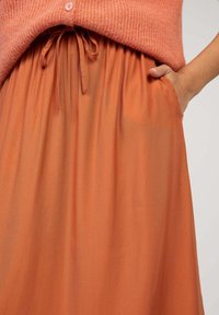 Jupe orange, légère, avec une taille froncée et un cordon de serrage. Dotée de poches latérales et d'une texture lisse.