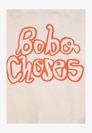 Tissu beige avec un grand texte orange ondulé indiquant « Bobo Choses » en lettres arrondies et ludiques.