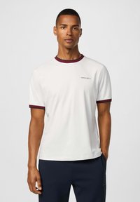 Biele tričko s krátkym rukávom a bordovým rebrovaným golierom a manžetami, s malým logom "HACKETT" na ľavej strane hrude.