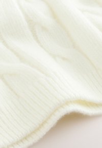 Tessuto bianco lavorato a maglia con una texture a coste e un sottile motivo a treccia. Fibre morbide e pelose creano un aspetto caldo e accogliente.